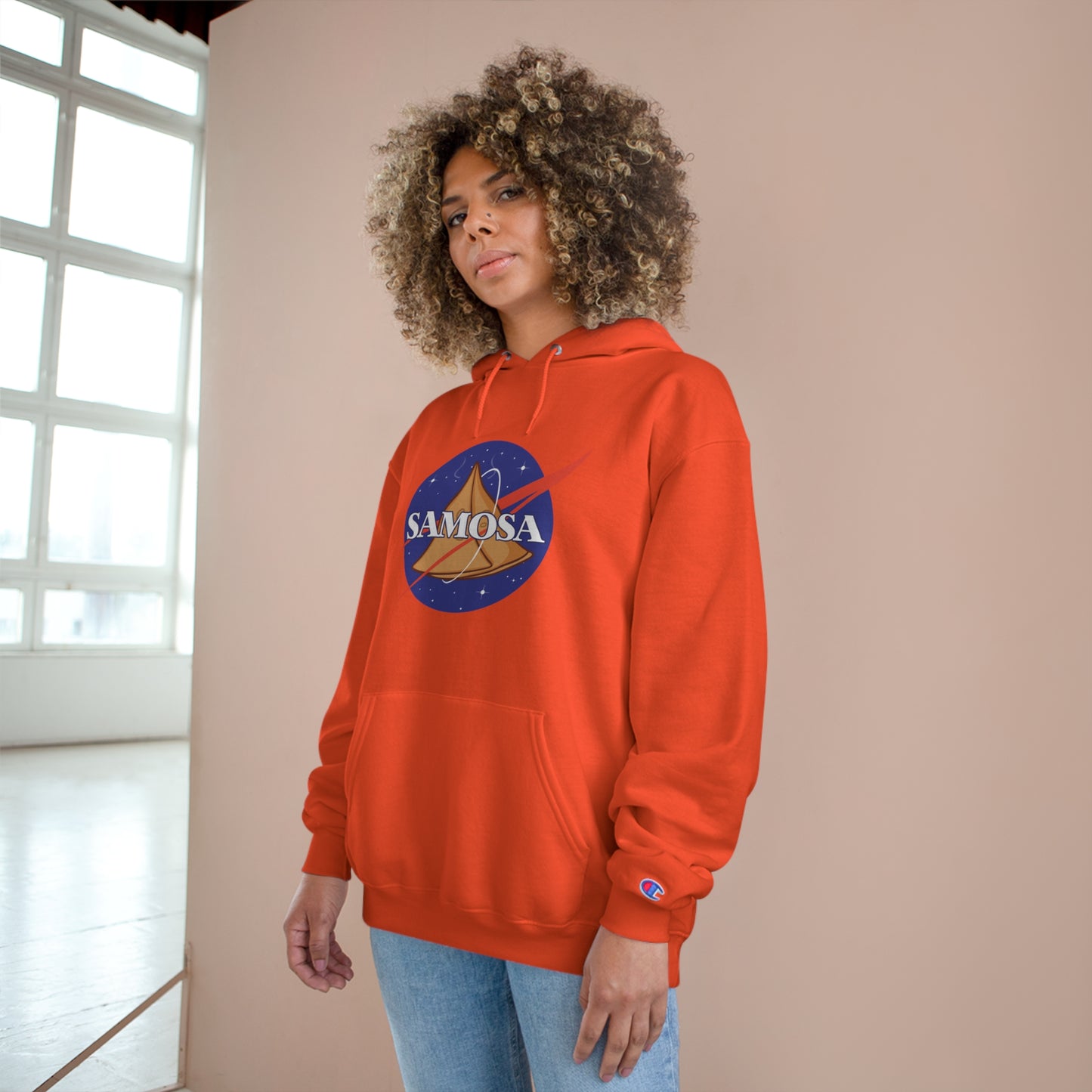 Woman wearing NASA Samosa Champion hoodie in vibrant orange, featuring a spacious pocket and logo design.