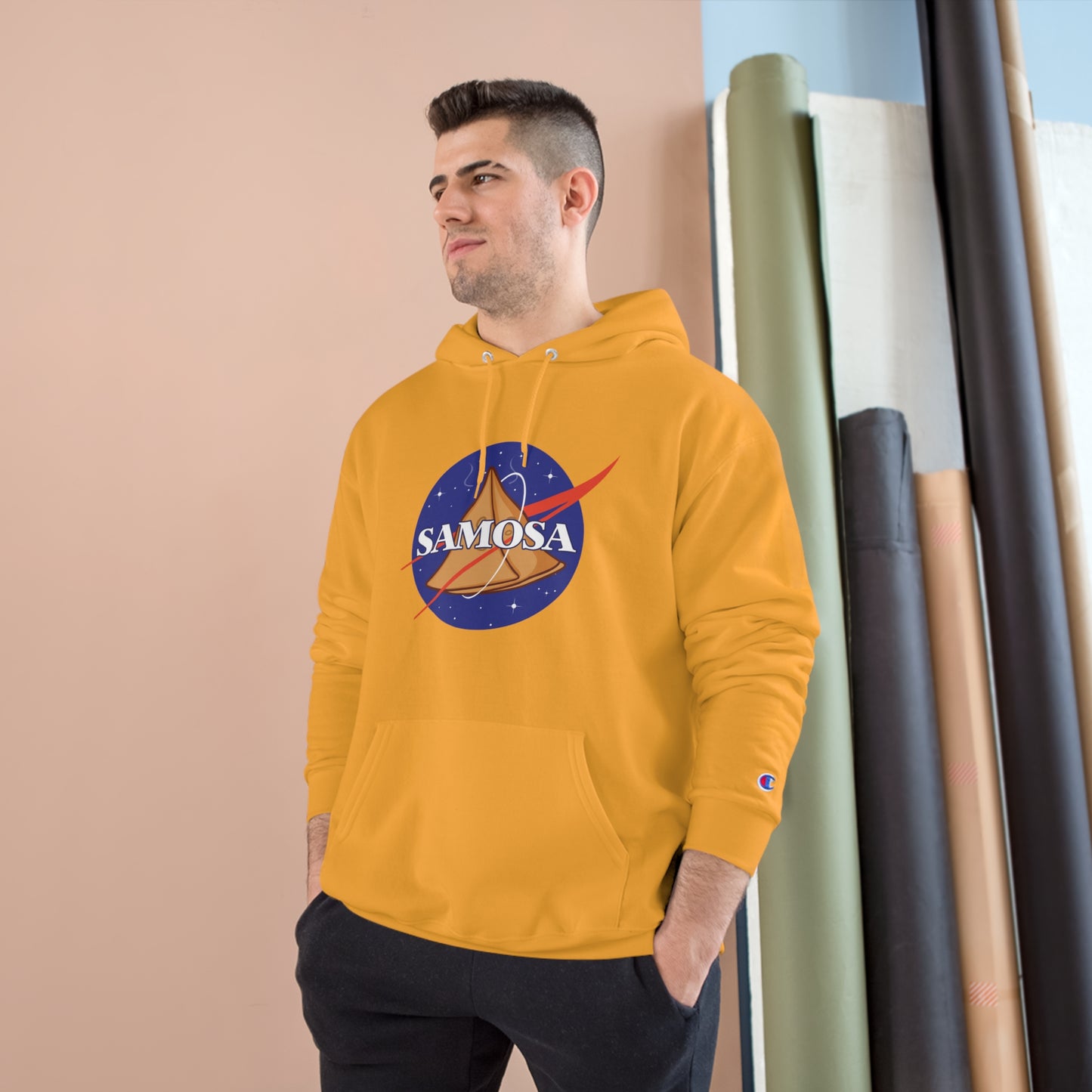 Young man wearing yellow NASA Samosa Champion hoodie with spacious pocket against a neutral background.