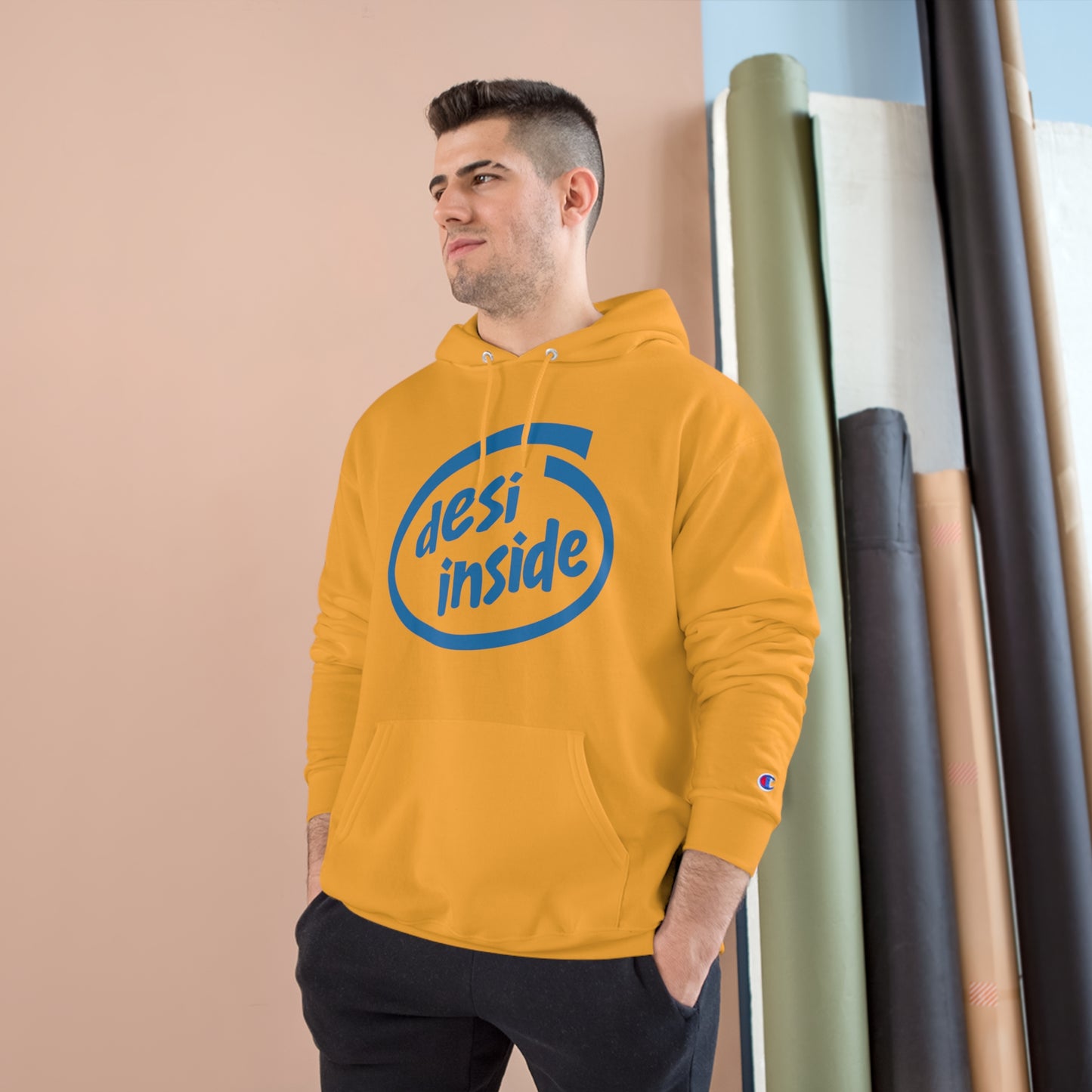 Model wearing a yellow 'Desi Inside' Champion hoodie with spacious pocket and iconic logo against a neutral backdrop.