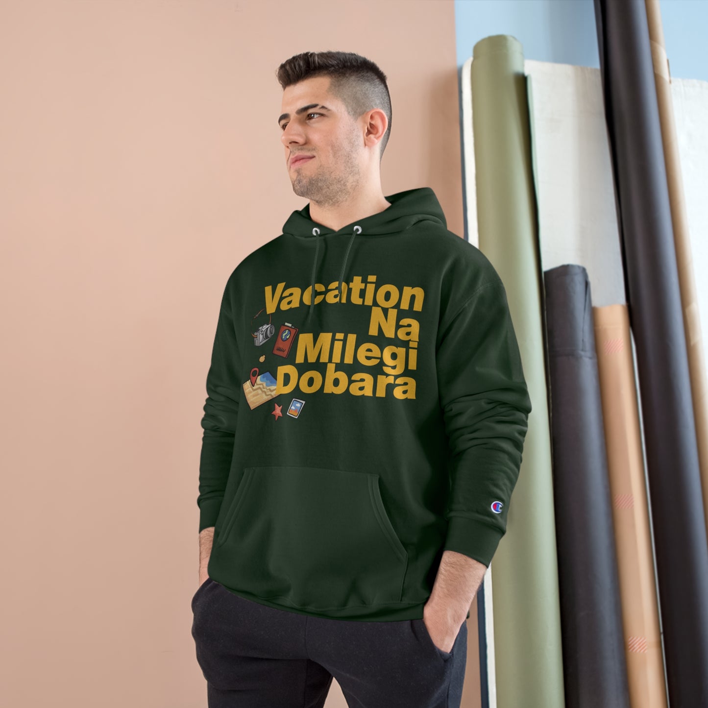 Man wearing a dark green VNMD Champion hoodie with travel-themed graphics, perfect for adventure seekers and cozy comfort.