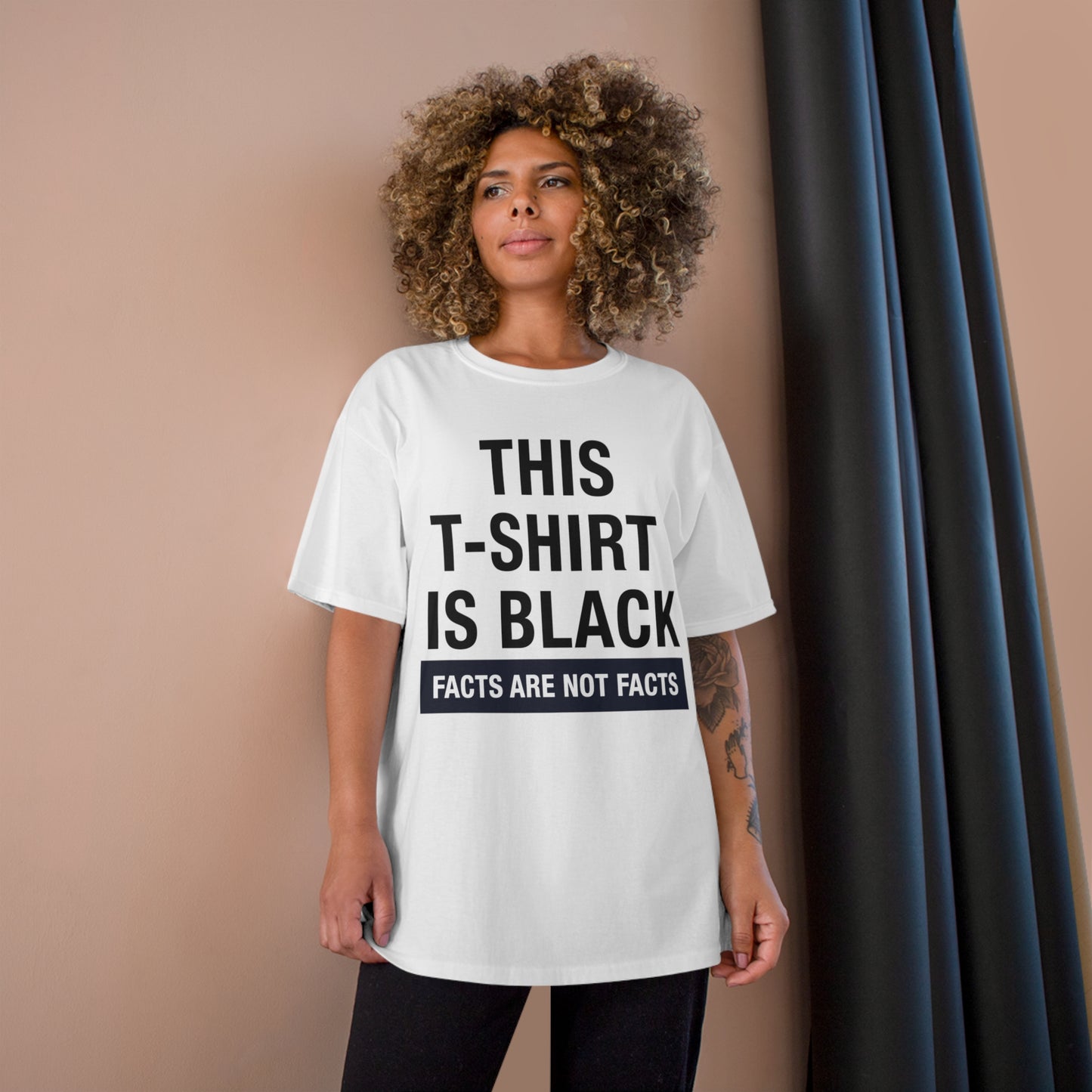 Woman wearing a white oversized t-shirt with bold text that humorously states, "THIS T-SHIRT IS BLACK."
