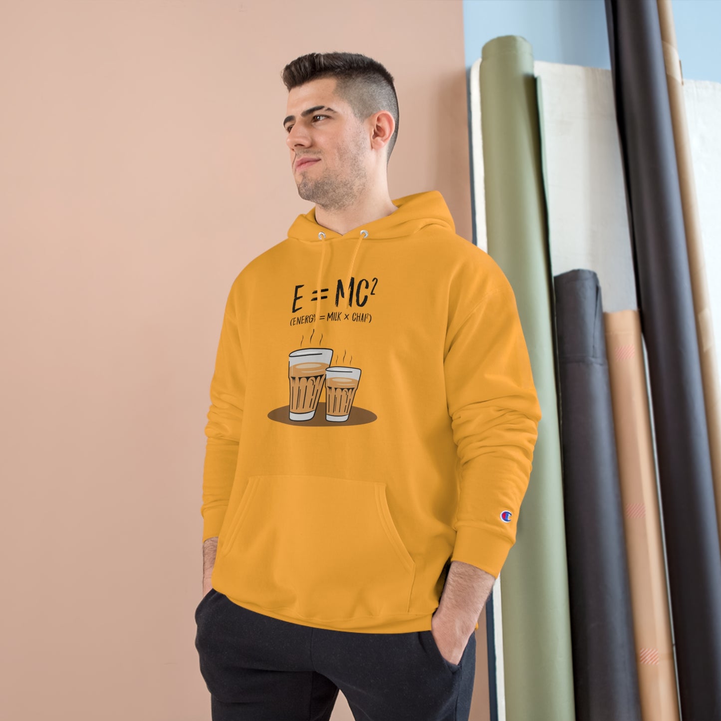Man wearing E=MC² Champion hoodie in mustard, featuring chai graphic and cozy design for comfort.