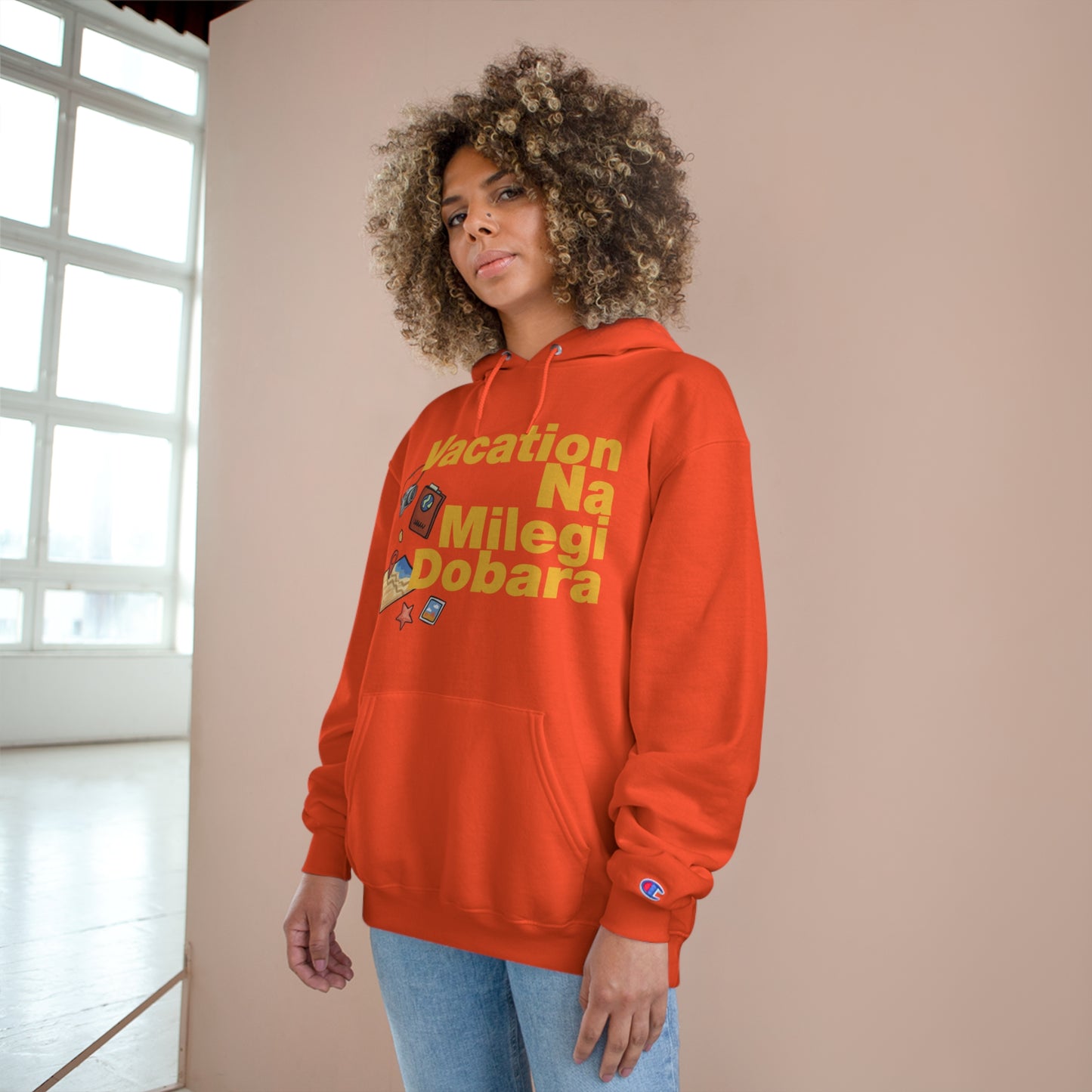 Woman wearing an orange VNMD Champion hoodie with "Vacation Na Milegi Dobara" graphic and spacious pocket.